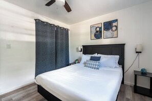 Ein Schlafzimmer mit einem Bett, einem dunklen Kopfteil, einem Nachttisch, einer Wandlampe und einem Deckenventilator.