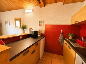Eine kompakte Küche mit Holzschränken, einer schwarzen Arbeitsplatte und einer roten Spritzschutzwand.