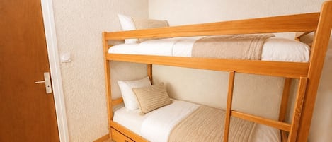 A bunk bed with a wooden frame, white bedding, and a beige throw blanket.