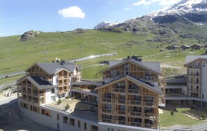 Ein modernes Hotel mit Holzfassade, mehreren Balkonen und Blick auf eine Berglandschaft.