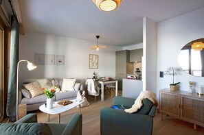 A modern living room with a sofa, coffee table, and chairs, a dining area with a table and chairs, and a kitchen in the background. - Ski aux pieds | Vue imprenable | Piscine & Spa (Alpe d'Huez)