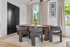 A dining area with a round table, four grey upholstered chairs, a beige rug, and a black door. - NEW Luxury home with rooftop hot tub and spa like bathroom (Nashville)