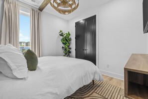 A bedroom with a bed, a wooden nightstand, a black door, and a window with curtains. - NEW Luxury home with rooftop hot tub and spa like bathroom (Nashville)