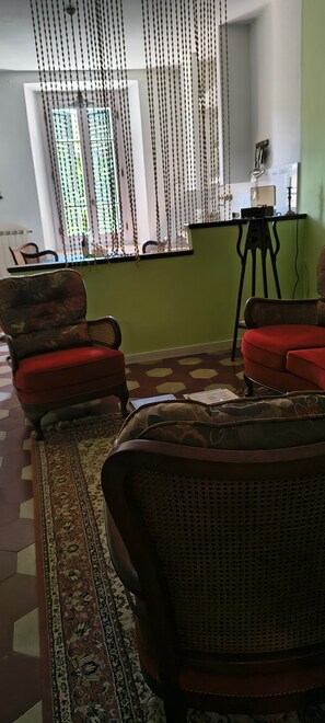 Une pièce comprenant deux fauteuils, un tapis à motifs, un trépied et une fenêtre avec des stores.