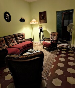 Ein Wohnzimmer mit einem roten Sofa, einem gemusterten Sessel, einem kleinen Tisch mit einer Lampe und einem Boden mit sechseckigen Fliesen.