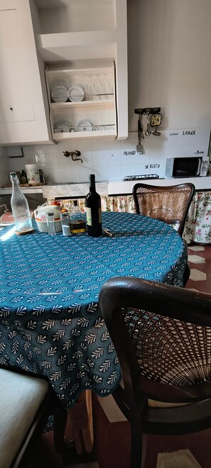 Ein Essbereich mit einem runden Tisch, der mit einer gemusterten Tischdecke bedeckt ist, umgeben von Korbstühlen.