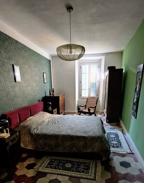 Ein Schlafzimmer mit einem Bett, einem Schreibtisch, einem Sessel, einem Fenster und einer Hängeleuchte.