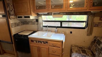 Uma cozinha compacta para motorhome, com fogão, pia e armários de madeira.