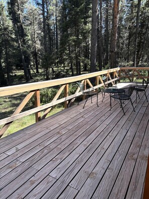 A wooden deck with metal chairs and a table, surrounded by a forest.