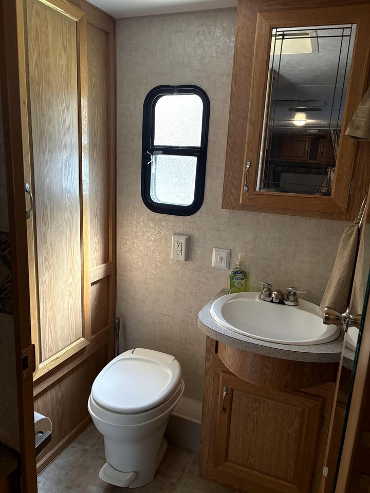 A compact bathroom with a toilet, a sink, and wooden cabinets.