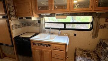 Uma cozinha compacta para motorhome, com fogão, pia e armários de madeira.