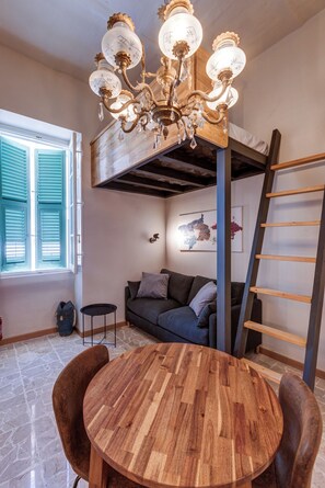 Une pièce chaleureuse avec une table à manger en bois, un canapé, un lustre et une échelle appuyée contre le mur.