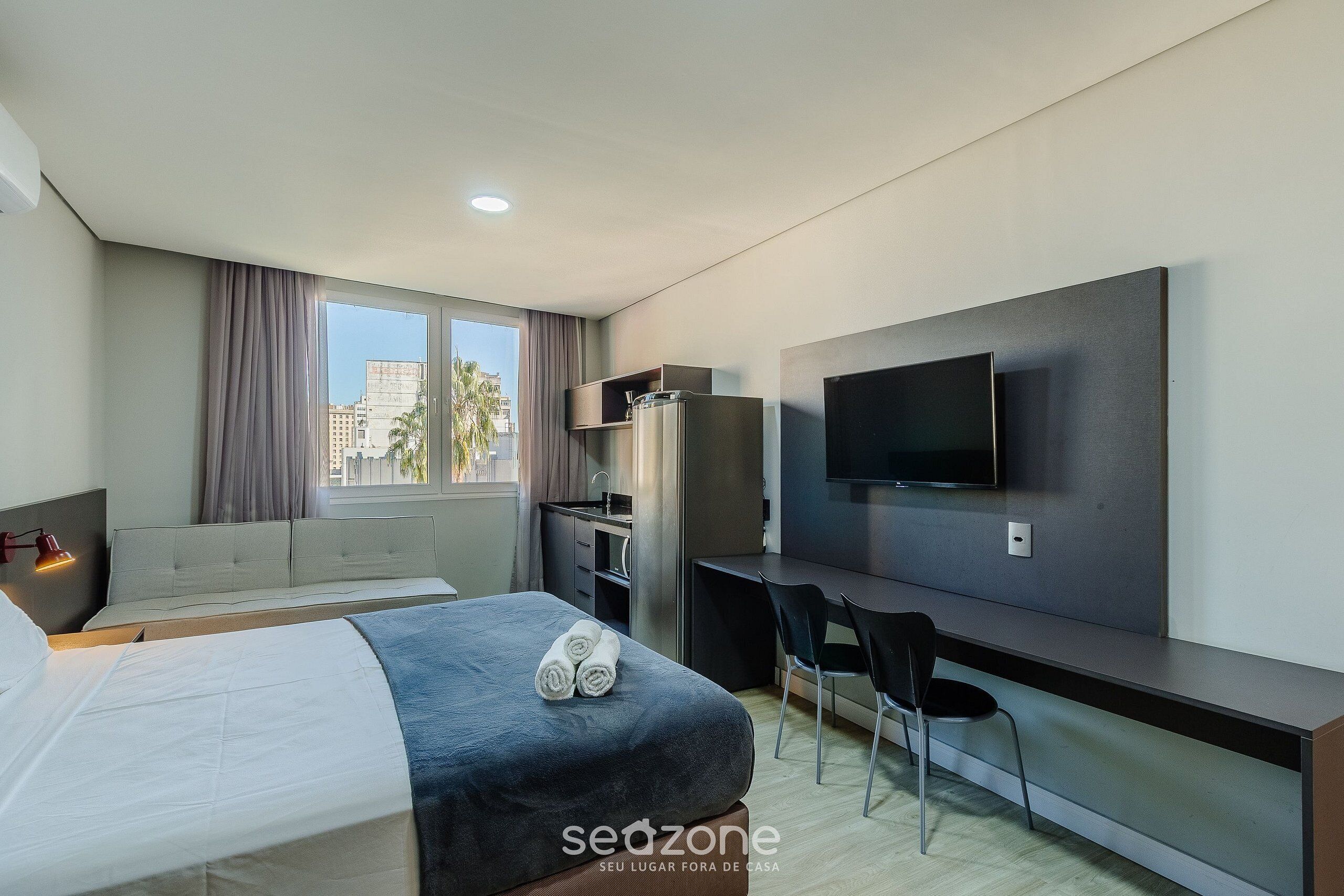 Ein modernes Hotelzimmer mit Bett, Schreibtisch, Stuhl, Fernseher und einem Fenster mit Vorhängen.