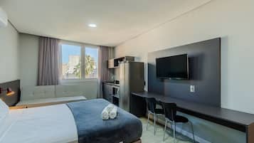Ein modernes Hotelzimmer mit Bett, Schreibtisch, Stuhl, Fernseher und einem Fenster mit Vorhängen.