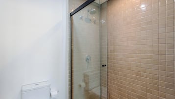 A bathroom with a glass shower enclosure, a white toilet, and beige tiled walls.