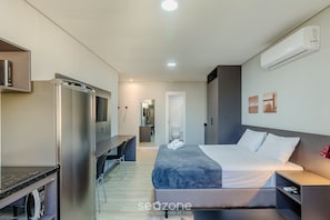 A modern hotel room with a bed, a desk, a microwave, and an air conditioning unit. - Studio Downtown Near Ccmq - Tco0501 (Porto Alegre)