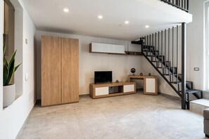 A modern living room with a TV, wooden cabinet, and a staircase. - The Urban Nest Comfort Suite (Bari)