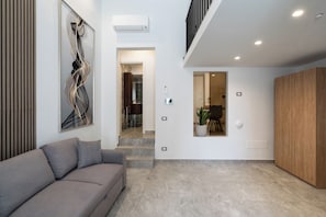 A modern living room with a grey sofa, a large abstract painting, and a wooden cabinet. - The Urban Nest Comfort Suite (Bari)