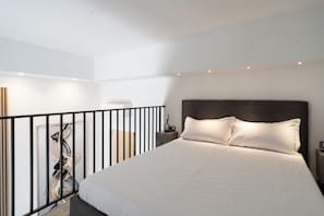 A modern hotel room with a large bed, a nightstand, and a view of the balcony. - The Urban Nest Comfort Suite (Bari)