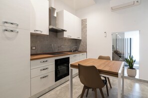 A modern kitchen with white cabinetry, a wooden countertop, and a built-in oven. There is a dining table with chairs and a potted plant. - The Urban Nest Comfort Suite (Bari)