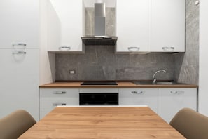 A modern kitchen with white cabinets, a wooden countertop, a stainless steel range hood, and a built-in dishwasher. - The Urban Nest Comfort Suite (Bari)