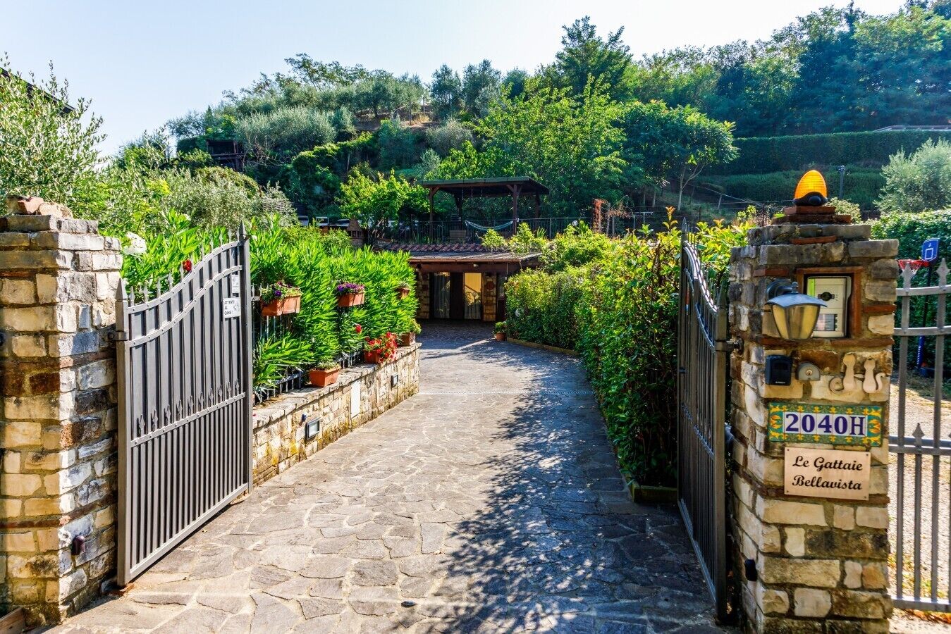 A stone pathway leading to a gated entrance with a sign reading 'Le Gattaie Bellavista.'