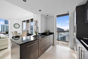 Eine moderne Küche mit einer großen Kochinsel, einem Essbereich mit Tisch und Stühlen sowie einem Blick auf die Stadt durch große Fenster.