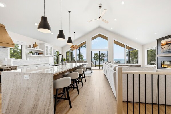 Una cocina moderna con encimera de mármol, lámparas colgantes negras y una isla grande con taburetes de bar.