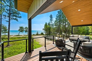 Una terraza de madera con mobiliario exterior con vista a una playa y un bosque.