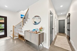 A modern interior with a staircase, a round mirror, a desk with items, and a door.