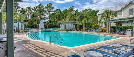 A swimming pool with lounge chairs and a covered area, surrounded by trees and a building.