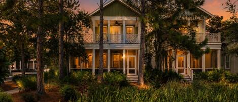 A two-story house with a balcony, surrounded by trees and vegetation.