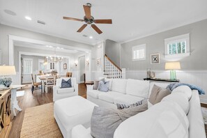 Ein geräumiges Wohnzimmer mit einem weißen Sofa, einem Essbereich und einer Treppe.