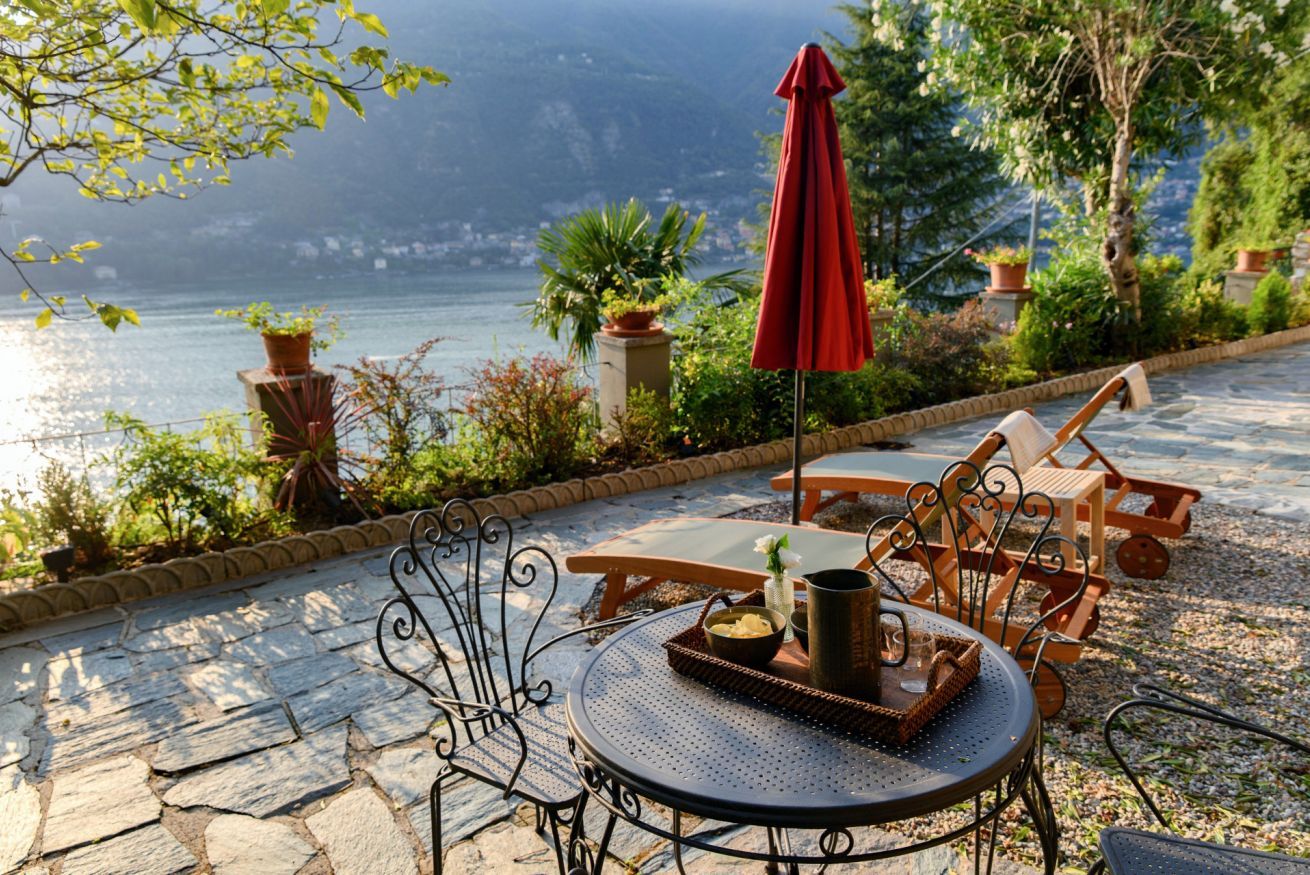 An outdoor patio with a round table, chairs, and a red umbrella.