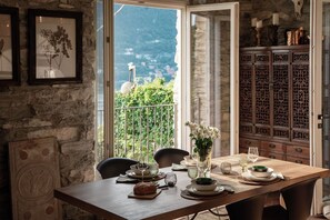 A dining area with a table set for two, a stone wall, and a view of greenery and mountains through an open door. - Villa La Solitaria - My Home in Como (Blevio)