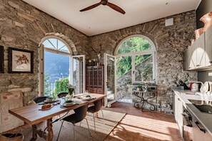 A stone-walled room with a dining table, chairs, and a ceiling fan. - Villa La Solitaria - My Home in Como (Blevio)