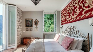Ein Schlafzimmer mit einem Bett, einem Fenster, einer Steinwand und Blick ins Grüne.