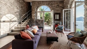 Ein Zimmer mit Steinwänden, einer Treppe, einem Sofa, einem Couchtisch und Korbstühlen.