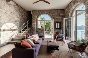 A stone-walled room with a staircase, a sofa, a coffee table, and wicker chairs. - Villa La Solitaria - My Home in Como (Blevio)