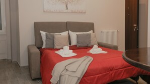 Una habitación de hotel con una cama, una mesita pequeña, un radiador y una puerta.