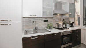 Una cocina moderna con muebles blancos, un lavamanos de acero inoxidable, una estufa a gas y un horno empotrado.