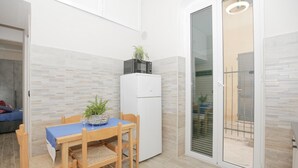 Une cuisine compacte comprenant une table à manger, des chaises, un réfrigérateur et une porte-fenêtre coulissante donnant sur un espace extérieur.