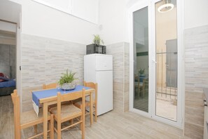 A compact kitchen with a dining table, chairs, a refrigerator, and a sliding glass door leading to an outdoor area. - Maison Sirivle 7.2 Apartment with Private Terrace and Wi-Fi (Genoa)