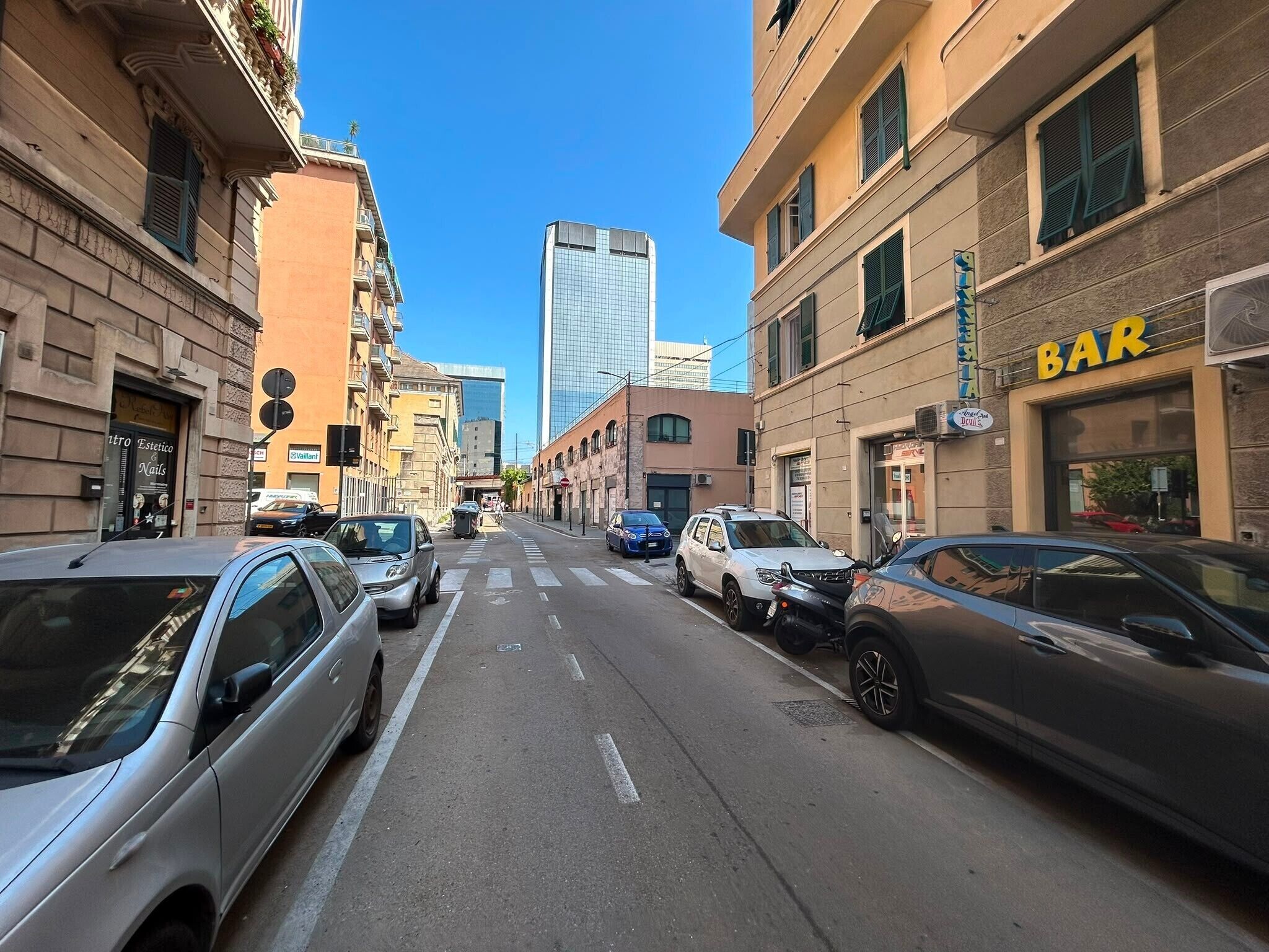 Straßenansicht mit parkenden Autos, einer Bar und Gebäuden mit unterschiedlichen Schildern.