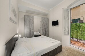 Une chambre à coucher avec un lit, une télévision, une armoire et un balcon agrémenté d’une clôture verte.