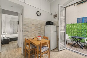 A compact living space with a kitchenette, a dining area with a table and chairs, a bed, and a view of a green outdoor area. - Maison Sirivle 7.2 Apartment with Private Terrace and Wi-Fi (Genoa)