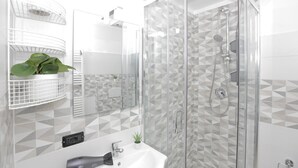 Une salle de bain moderne avec une douche à parois de verre, un lavabo blanc et des carreaux aux motifs géométriques.
