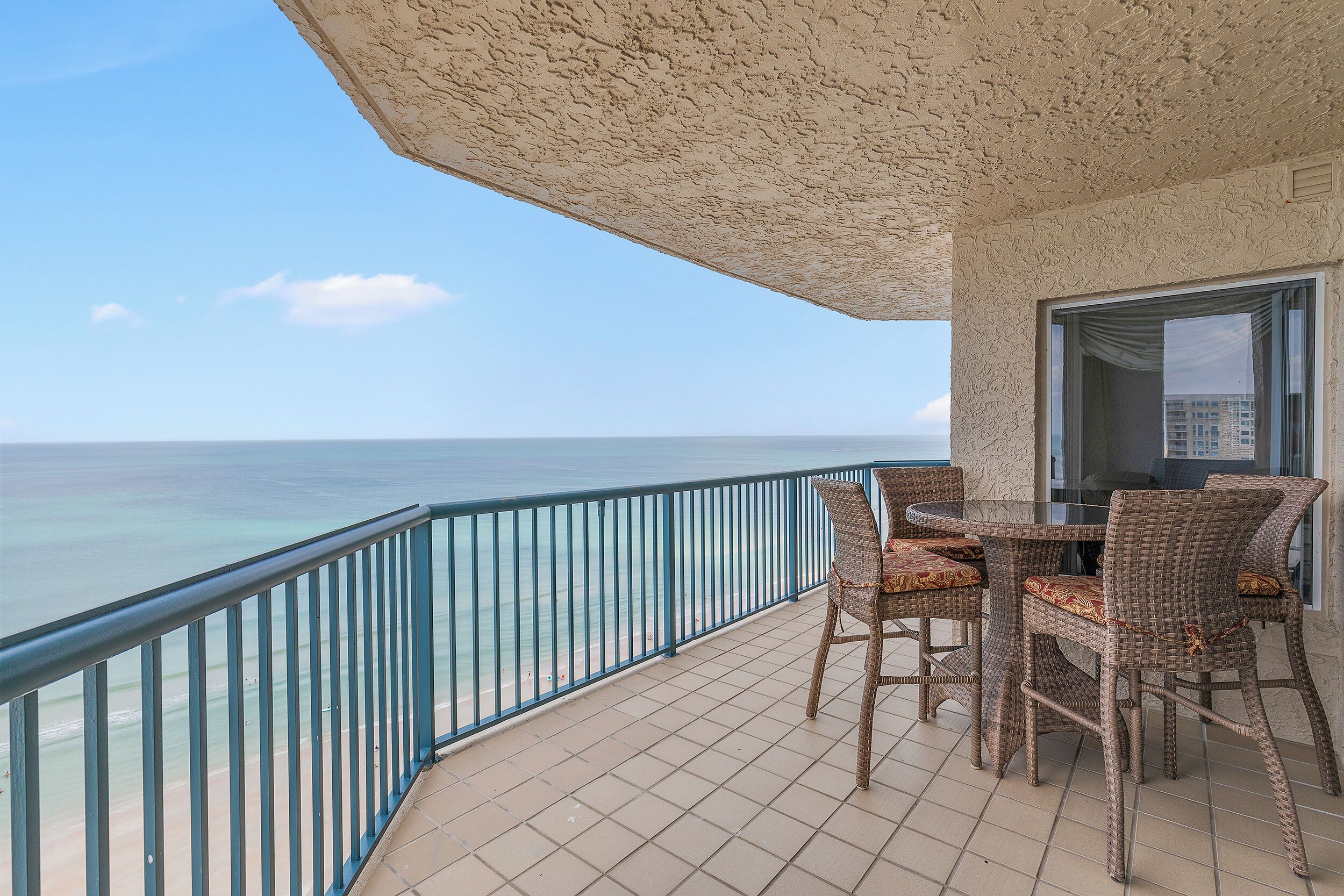 A balcony with a view of the ocean, featuring wicker furniture and a tiled floor.
