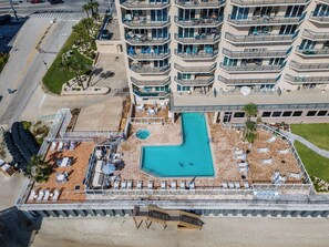 Ein mehrstöckiges Hotel mit Pool auf dem Dach, Außenbereich zum Sitzen und Strandabschnitt.