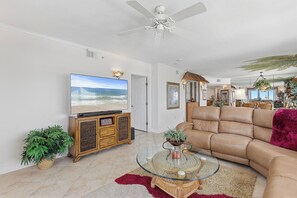 A living room with a television, sofa, and a ceiling fan. - 🌴Panoramic Ocean + River Views 19th Floor Corner Condo - Towers Ten 1901 (Daytona Beach Shores)